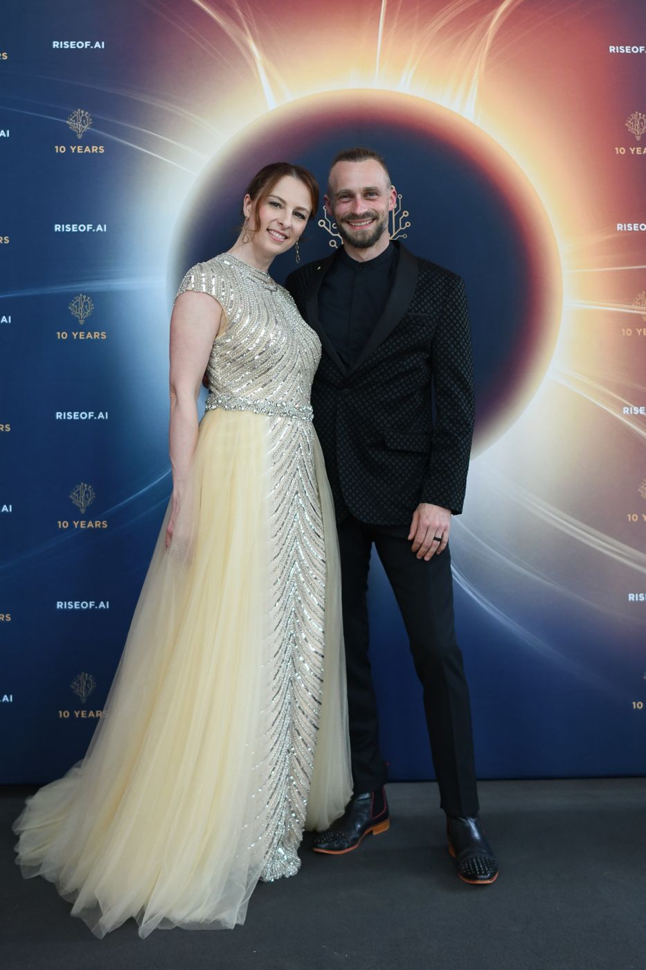 Veronika im goldenen Abendkleid mit Fabian vor der Jubiläumswand