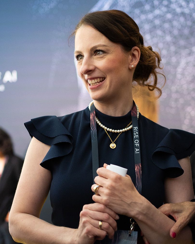 Veronika Westerheide mit verschränkten Armen vor der Fotowand der Rise of AI